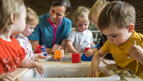 Kinderbegeleidster en kinderen spelen in een zandbak