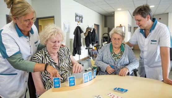 Twee oudere vrouwen in een dagopvang samen met hun verzorgenden